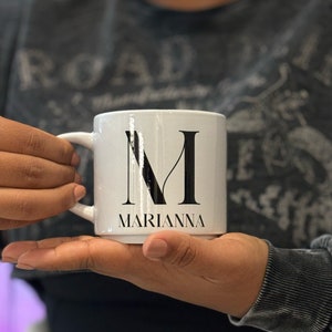 May include: White ceramic mug with a black letter "M" and the name "MARIANNA" printed on the front.