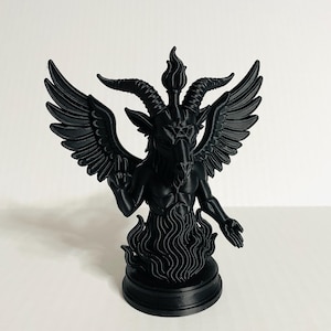May include: A black statue of Baphomet, a goat-headed deity, with large wings, horns, and a torch between its horns. The statue is standing on a round base with flames at the bottom. The statue is a dark, solid color.