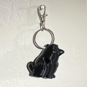 May include: A black 3D printed keychain shaped like a bird with a silver metal ring and clasp.