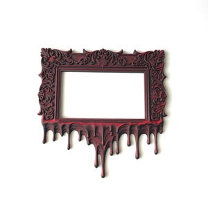May include: A rectangular picture frame featuring ornate, raised scrollwork patterns in a deep red and black color scheme. The bottom edge of the frame is designed with a distinct dripping effect, where the material appears to melt downward.