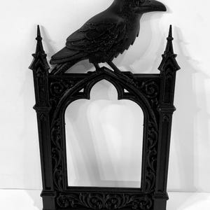 Puede incluir: Marco decorativo negro de estilo g&oacute;tico con un cuervo posado. El marco presenta una abertura arqueada y detalles ornamentados. El cuervo a&ntilde;ade un toque g&oacute;tico. El marco est&aacute; hecho de un material s&oacute;lido.