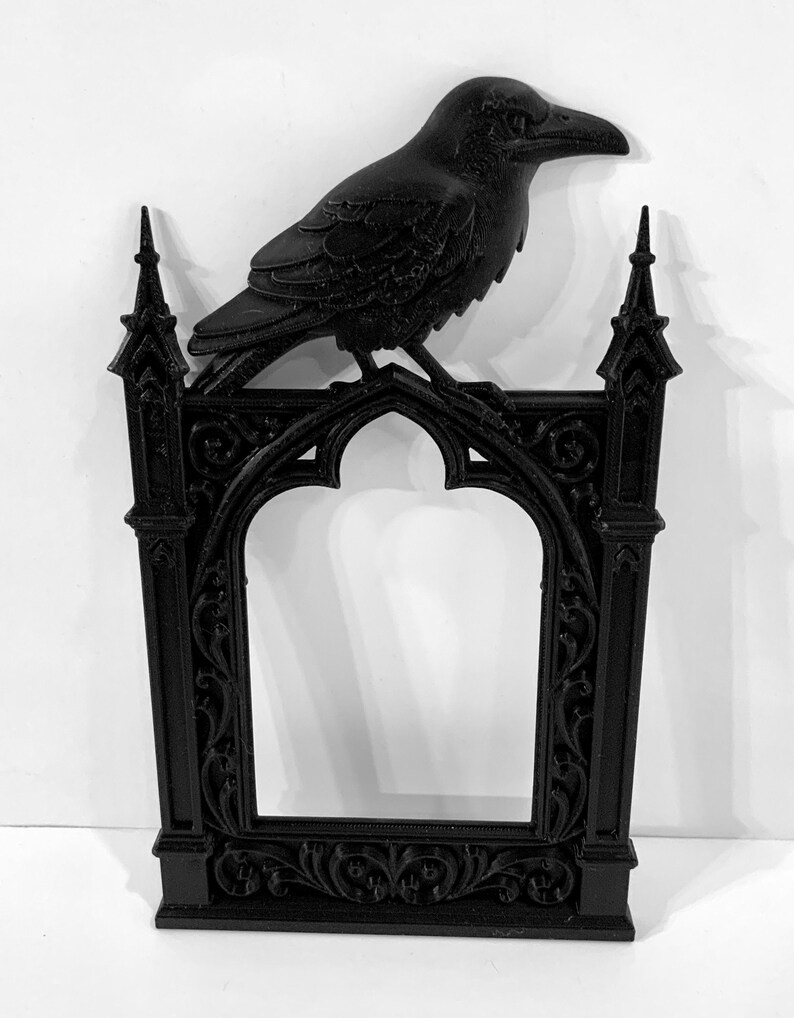 Puede incluir: Marco decorativo negro de estilo g&oacute;tico con un cuervo posado. El marco presenta una abertura arqueada y detalles ornamentados. El cuervo a&ntilde;ade un toque g&oacute;tico. El marco est&aacute; hecho de un material s&oacute;lido.