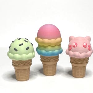 May include: Three colorful ice cream cones. One has a green scoop with black sprinkles, the second has a rainbow-colored scoop, and the third is pink with a cat face design. All cones are in a waffle cone.