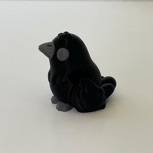 May include: A small, black, 3D printed bird figurine with a gray beak and eyes. The bird is sitting with its wings folded.