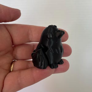 May include: A small, black, 3D printed figurine of a cartoon animal. The animal is sitting on its haunches with its head tilted up. The figurine is about 2 inches tall.
