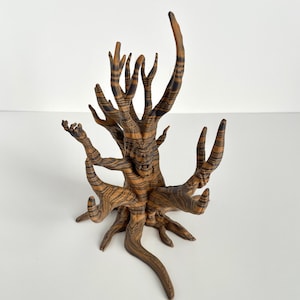 May include: A decorative tree sculpture with a detailed, textured design. The sculpture features a brown and black striped pattern, with multiple branches extending upwards and outwards. The tree is set against a white background.