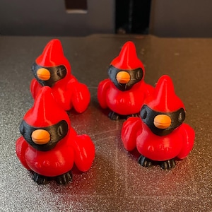 May include: Four red cardinal bird figurines with black masks and orange beaks. The figurines are made of a smooth, glossy material and have a realistic appearance.