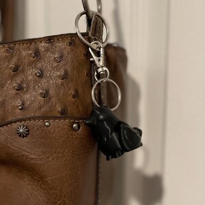 May include: A brown leather handbag with a silver chain and a black bird-shaped keychain.