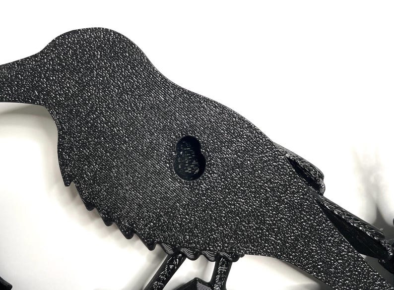 Puede incluir: Decoraci&oacute;n de pared con silueta de p&aacute;jaro de metal negro texturizado. El p&aacute;jaro tiene una superficie detallada y moteada y un ojal para colgar. El dise&ntilde;o presenta un p&aacute;jaro posado en una rama, adecuado para el hogar o el jard&iacute;n.