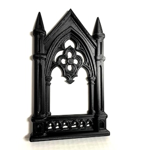 May include: A black gothic-style decorative frame with intricate architectural details. The frame features pointed arches, spires, and a quatrefoil design, creating a vintage aesthetic. The frame is made of a solid material.