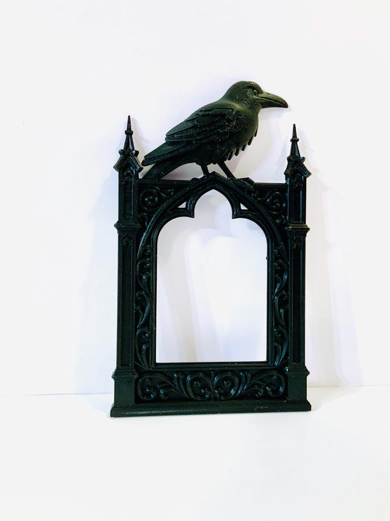 Puede incluir: Un marco decorativo verde oscuro con un dise&ntilde;o de arco g&oacute;tico, coronado por una detallada escultura de cuervo. El marco presenta adornos ornamentados y pin&aacute;culos puntiagudos, creando una est&eacute;tica vintage.