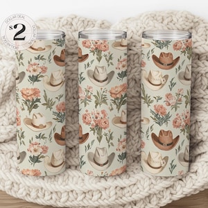 Op de afbeelding: Drie roestvrijstalen bekers met een bloemen- en cowboyhoedpatroon. De bekers staan op een wit gebreid deken. De tekst "$2 Dollar Deal" staat op een ronde sticker.