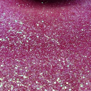 May include: Close-up of a vibrant pink glitter, with iridescent specks scattered throughout. The glitter is densely packed, creating a sparkling, textured surface. The image is well-lit, highlighting the reflective qualities of the glitter.
