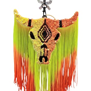 May include: A colorful, glittery bull skull keychain with a fringe of yellow and orange yarn.