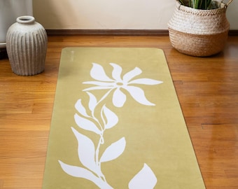 Puede incluir: Una esterilla de yoga amarilla con un diseño floral blanco. La esterilla está sobre un suelo de madera.
