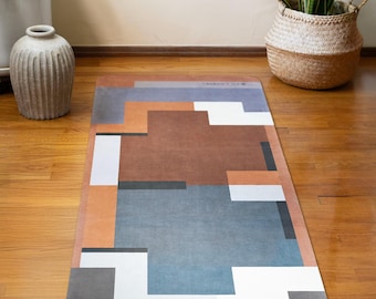 Puede incluir: Una esterilla de yoga con estampado geométrico en tonos marrones, azules, grises y blancos. La esterilla está colocada sobre un suelo de madera.