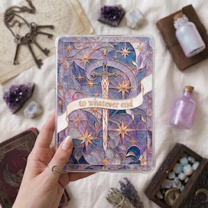 Può includere: Una custodia protettiva trasparente per tablet con un'illustrazione in stile vetrata raffigurante una spada al centro di motivi vorticosi blu e viola e stelle dorate, con un nastro bianco che riporta il testo to whatever end in oro.