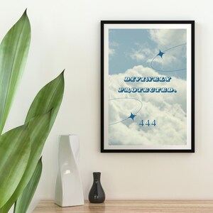Könnte beinhalten: Ein gerahmter Druck mit einem Hintergrund aus blauem Himmel und weißen Wolken. Der Text "DIVINELY PROTECTED. 444" ist in Blau auf dem Druck gedruckt.