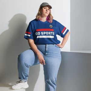 a blonde woman with pink hair tips and a baseball cap models a blue fan jersey. The design says "Go Sports" with red and white stripes.