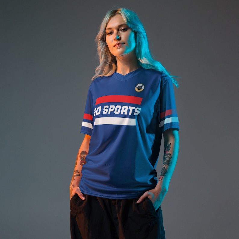an edgy blonde with tattoos models a blue sports fan jersey. The design says "Go Sports" with red and white stripes.