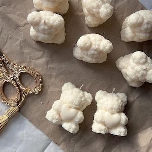 Könnte beinhalten: Eine Sammlung weißer, bärenförmiger Kerzen, einige mit einem kleinen Herzen. Die Kerzen sind aus weißem Wachs und haben eine strukturierte Oberfläche.