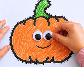 May include: A paper cutout of a pumpkin colored with orange crayon and a green stem, featuring a black outline and a dashed cutting line. Two plastic googly eyes are being placed onto the pumpkin, which has a black drawn smile.