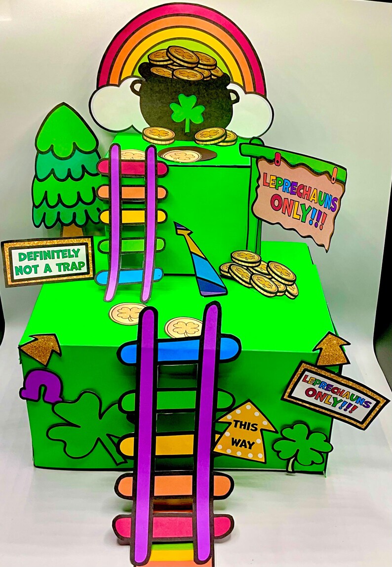 Op de afbeelding: Een groene doos met een regenboog en een pot goud er bovenop. Aan de zijkanten van de doos zijn twee ladders, een met regenboog treden en een met paarse treden. De doos heeft een bord met de tekst "Leprechauns Only!!" en een ander bord met de tekst "This Way".