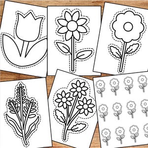 May include: A collection of black and white flower cutouts on white paper, including a tulip, daisy, and other floral designs. The cutouts are outlined with a dashed line, ready for crafting or coloring. The background is a wooden surface.