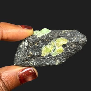 May include: A dark gray rock with light green mineral deposits. The rock has a rough texture, and the mineral formations are circular and clustered, with a vibrant, light green color. The background is a solid black.