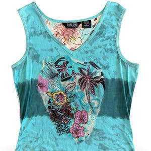May include: A turquoise sleeveless top with a V-neck and a floral and palm tree design. The top has a tie-dye effect and the text "TAKE TWO" is visible on the tag.