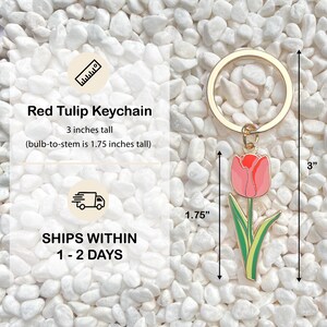 May include: A red tulip keychain with a gold-colored ring. The tulip is pink with red accents and green leaves. The keychain is 3 inches tall, with the bulb-to-stem measuring 1.75 inches. The text "Red Tulip Keychain" is visible.