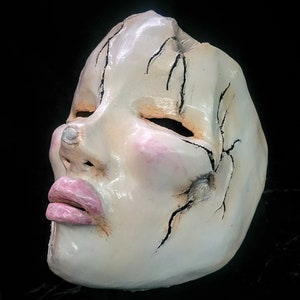 Peut inclure: Un masque en céramique blanche avec des fissures et une bouche peinte en rose. Le masque a un visage humain réaliste avec les yeux fermés.