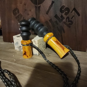May include: Two wooden jump ropes with black handles and yellow-toned wood handles. The handles are connected to a black and silver rope. The background features a wooden sign with text.