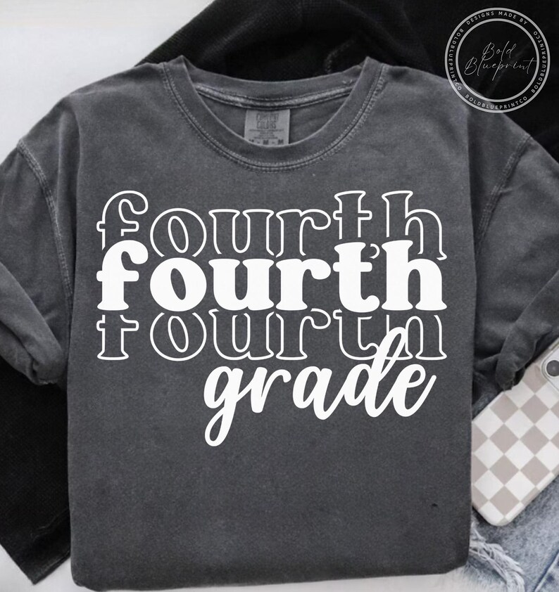 May include: Dark gray crew neck t-shirt with the words "fourth fourth fourth grade" in white, stacked vertically. The shirt has a vintage, washed look and a relaxed fit. A phone with a checkered case is visible.
