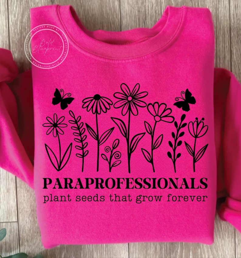 May include: Hot pink sweatshirt with a black floral design and two butterflies. The text "PARAPROFESSIONALS plant seeds that grow forever" is printed below the flowers. The sweatshirt is made of a soft material.