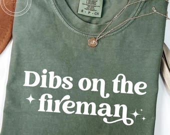 May include: A green t-shirt with the text "Dibs on the fireman" in white. The shirt has a distressed look and is made of a soft, comfortable fabric.