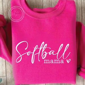 May include: A pink sweatshirt with the text "Softball mama" in white cursive lettering with a small heart.