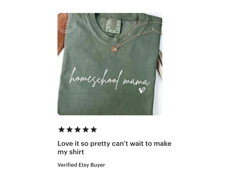May include: An olive green t-shirt with the words "homeschool mama" in white script, a small heart, and a delicate necklace. The shirt is folded, and the text is centered. The shirt is a casual wear item.