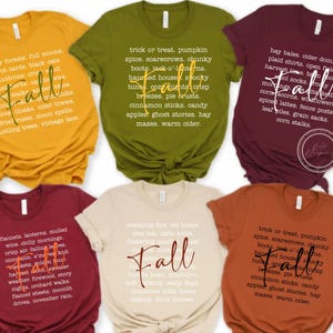 May include: Six colorful t-shirts with the word "Fall" and autumn-themed text graphics. Colors include mustard yellow, olive green, burgundy, cream, rust orange, and deep red. The shirts are casual wear.
