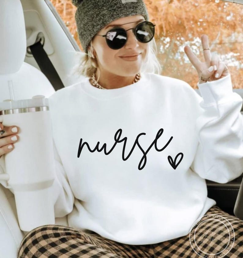 Peut inclure: Sweat-shirt blanc avec le mot "nurse" &eacute;crit en cursive noire avec un petit c&oelig;ur &agrave; c&ocirc;t&eacute;.