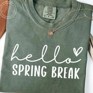 May include: A green t-shirt with the text "hello spring break" in white lettering with a small heart next to the word "hello".