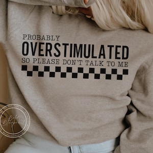 May include: A gray sweatshirt with black text that reads "Probably Overstimulated So Please Don't Talk To Me" with a black and white checkered pattern below the text.