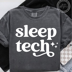 May include: Dark gray crew neck sweatshirt with the words "sleep tech" in large white letters. Two white starbursts are to the right of the word "tech". The sweatshirt is folded.