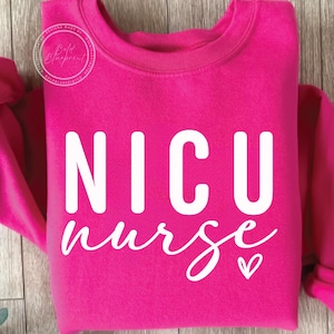 Puede incluir: Una sudadera rosa brillante con el texto "NICU nurse" en letras blancas y un pequeño corazón blanco.