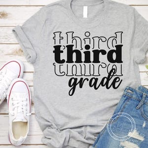 May include: A light gray t-shirt with the words "third grade" in a black, bold font. The shirt is paired with denim shorts and white sneakers with red trim. The shirt is likely for a student.