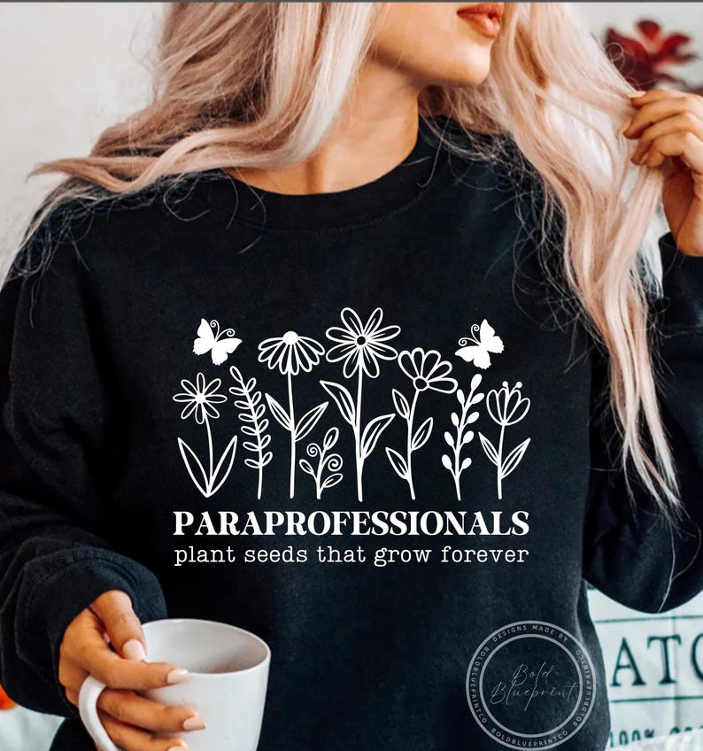 May include: Black sweatshirt with a white floral design and the text "PARAPROFESSIONALS plant seeds that grow forever." The design includes butterflies and various flower illustrations.