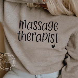 May include: A gray sweatshirt with the text "massage therapist" and a small heart printed on the front.