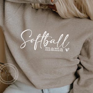 May include: A gray sweatshirt with the text "Softball Mama" in white cursive lettering with a small heart.