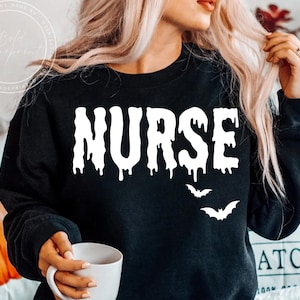 May include: Black sweatshirt with the word "NURSE" in dripping white letters, with three white bat silhouettes below. The sweatshirt is a Halloween-themed design.