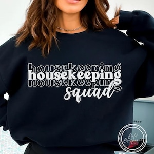 May include: Black sweatshirt with the words "housekeeping squad" in white, stacked vertically. The text has a layered effect, with a slight shadow. The sweatshirt is a crew neck style.